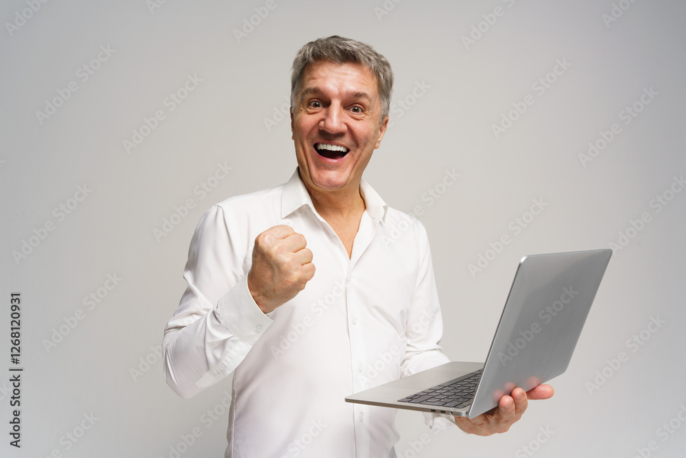 Elderly man celebrates success while holding a laptop in a neutral studio setting Elderly man celebrates success while holding a laptop in a neutral studio setting