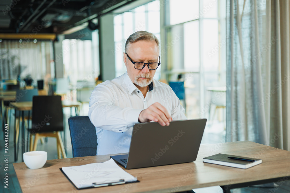 A businessman works diligently on his laptop in a modern office with a creative atmosphere A businessman works diligently on his laptop in a modern office with a creative atmosphere