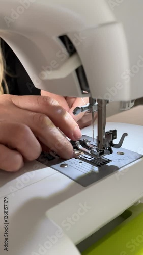 Close-up of a sewing machine in action, with a woman’s hand guiding fabric. The needle is shown stitching through the cloth, highlighting the intricate process of sewing with precision and care. photo