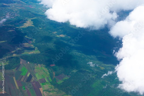 Obraz na płótnie Aerial view of a lush green landscape with agricultural fields and dense forests, partially covered by fluffy white clouds casting shadows below. Mix of cultivated land and vibrant vegetation w salonie