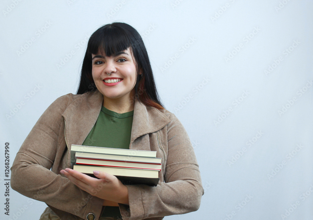 Smiling female university student holding a stack of books on her arms. She wears a green shirt and brown jacket, neutral background. Ideal for education, library, teaching, learning, reading. Smiling female university student holding a stack of books on her arms. She wears a green shirt and brown jacket, neutral background. Ideal for education, library, teaching, learning, reading.
