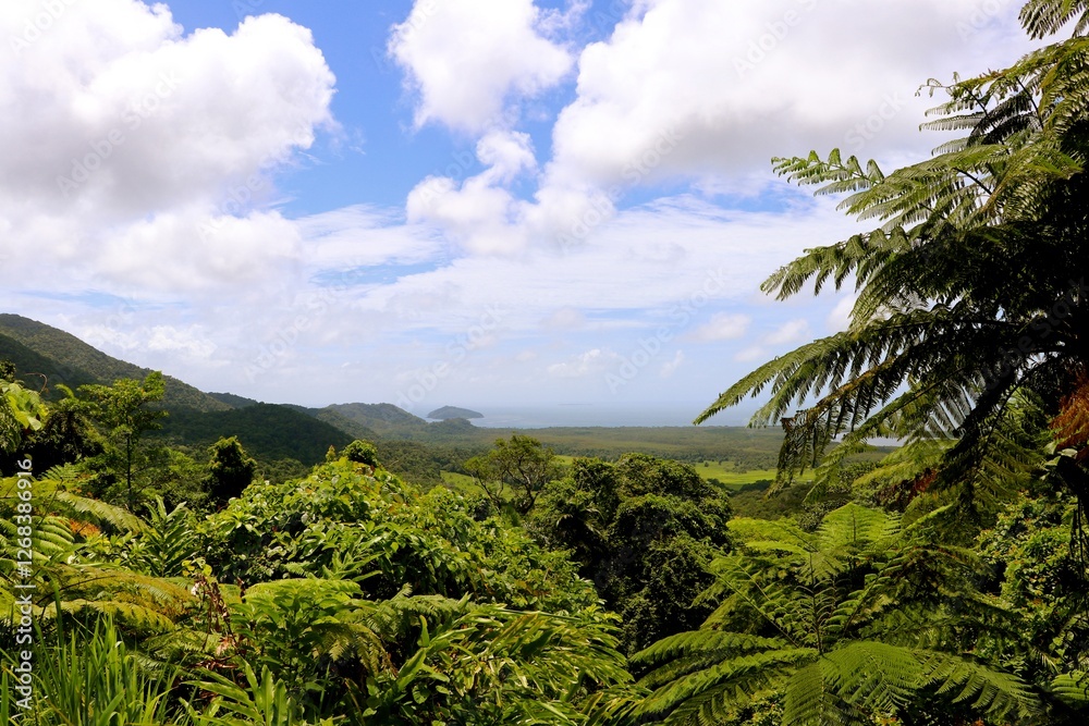 Vibrant green mountains create a breathtaking view, framed by flourishing foliage. The bright blue sky and soft clouds add to the tranquility of this natural paradise at midday