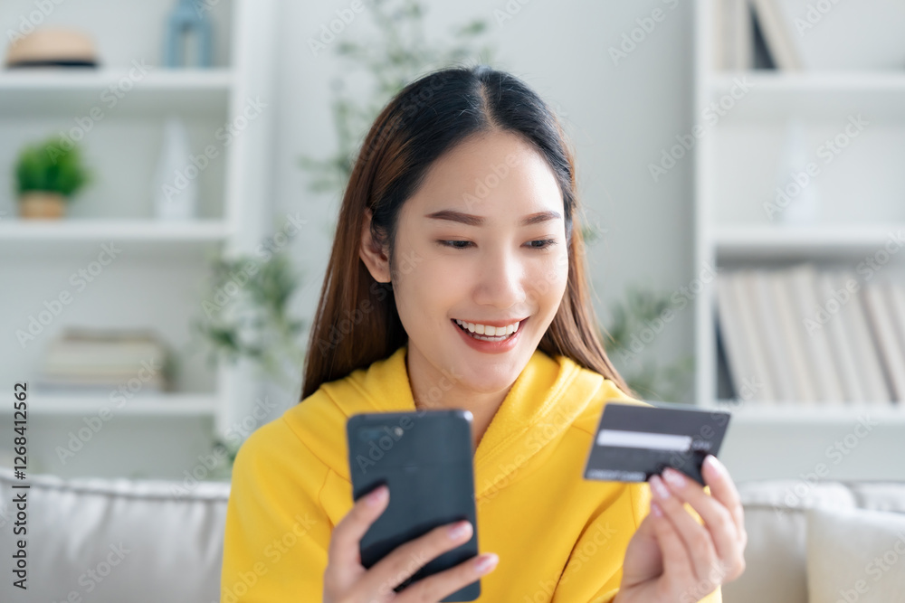 Young asian woman lying on sofa in living room, makes online banking payments through the internet from bank card on cell phone. Shopping online on mobile with credit card