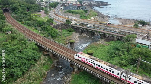 Aerial view of a Puyuma Express train dashing across a river by the mountainside and a coastal highway running through a seaside village, in Toucheng Township, Yilan County, Taiwan
