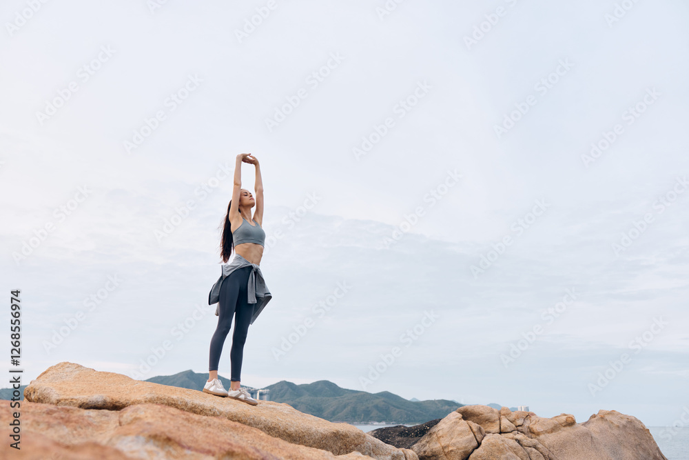 Young woman stretching outdoors on rocks, wearing athletic sportswear and enjoying a moment of tranquility in nature, embodying health and fitness concepts Young woman stretching outdoors on rocks, wearing athletic sportswear and enjoying a moment of tranquility in nature, embodying health and fitness concepts