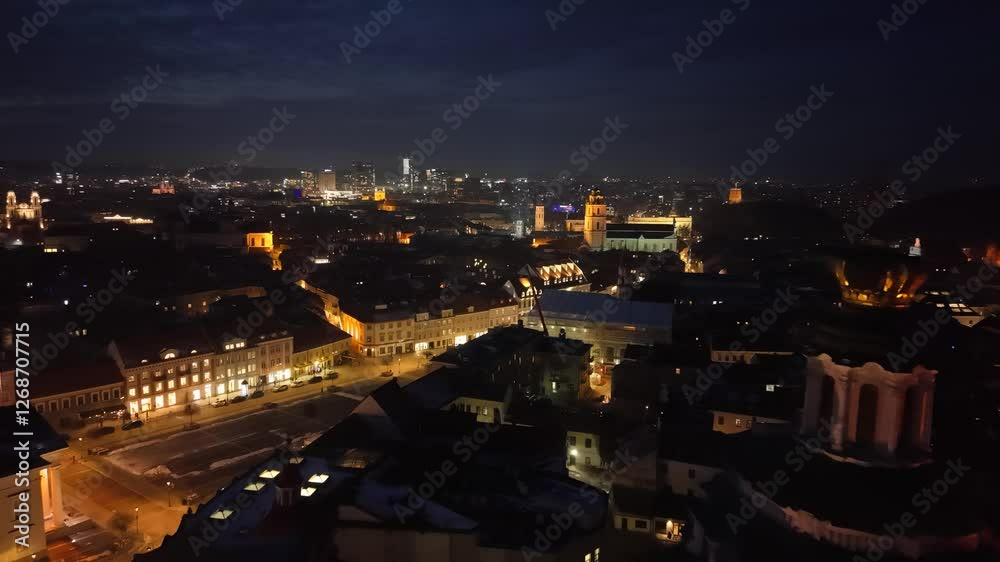Illuminated night view of Vilnius, Lithuania, showcasing a blend of historic landmarks and modern skyscrapers in the cityscape. Illuminated night view of Vilnius, Lithuania, showcasing a blend of historic landmarks and modern skyscrapers in the cityscape.