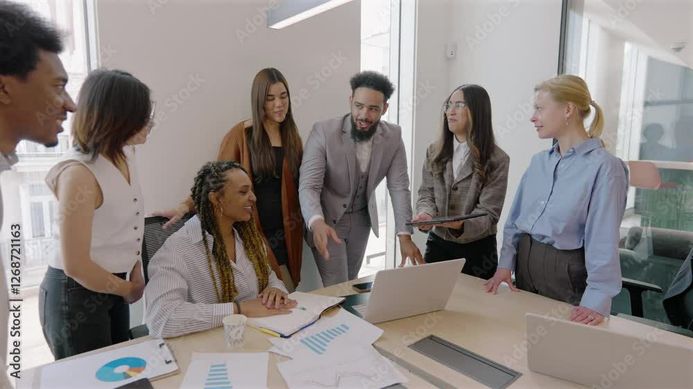 In a modern office, a diverse group of professionals engages in animated discussion around a laptop, highlighting the importance of teamwork in achieving their collective business goals