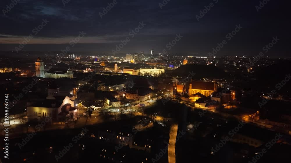 Illuminated night view of Vilnius, Lithuania, showcasing a blend of historic landmarks and modern skyscrapers in the cityscape. Illuminated night view of Vilnius, Lithuania, showcasing a blend of historic landmarks and modern skyscrapers in the cityscape.