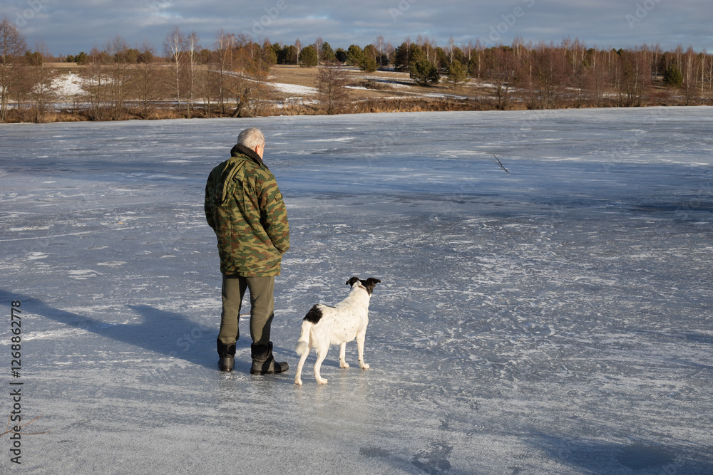 Naklejka premium A man with a dog on the ice of a frozen dam