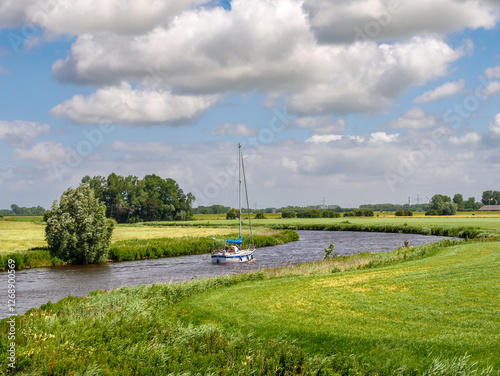 Sailboat on meandering Reitdiep river in rural Groningen, Netherlands, surrounded by farmland and grassland