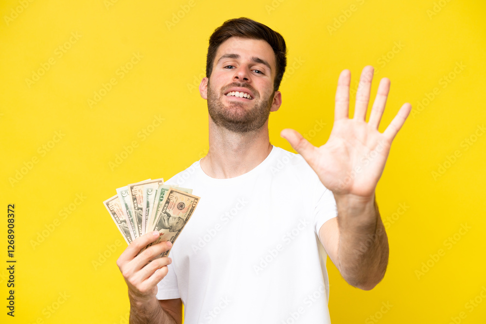 Young caucasian man taking a lot of money isolated on yellow background counting five with fingers Young caucasian man taking a lot of money isolated on yellow background counting five with fingers
