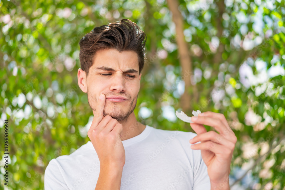 Young caucasian man at outdoors holding invisible braces with pain Young caucasian man at outdoors holding invisible braces with pain