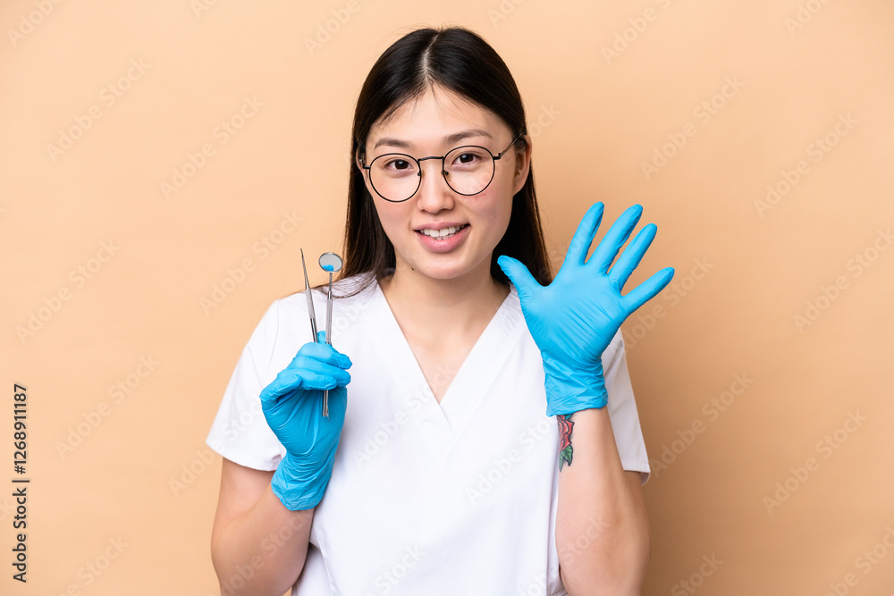 Dentist Chinese woman holding tools isolated on beige background counting five with fingers Dentist Chinese woman holding tools isolated on beige background counting five with fingers