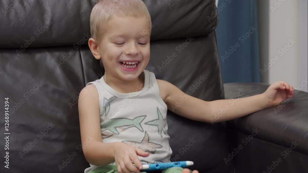 Happy child sitting on sofa playing on digital tablet. Smiling face of little boy engaged in playing tablet game for kids.