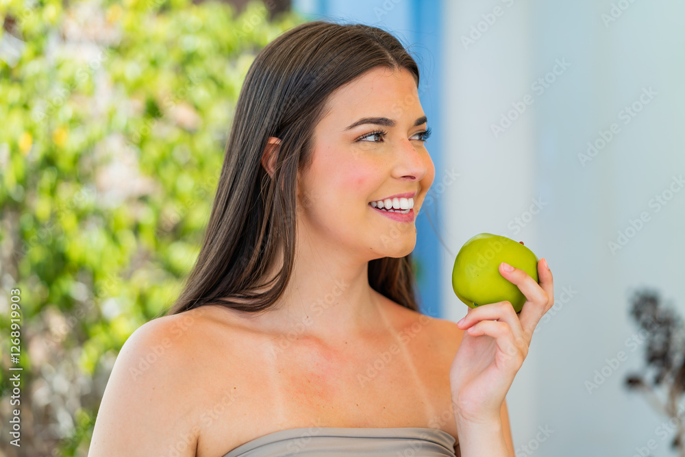 Young pretty Brazilian woman at outdoors holding an apple with happy expression Young pretty Brazilian woman at outdoors holding an apple with happy expression
