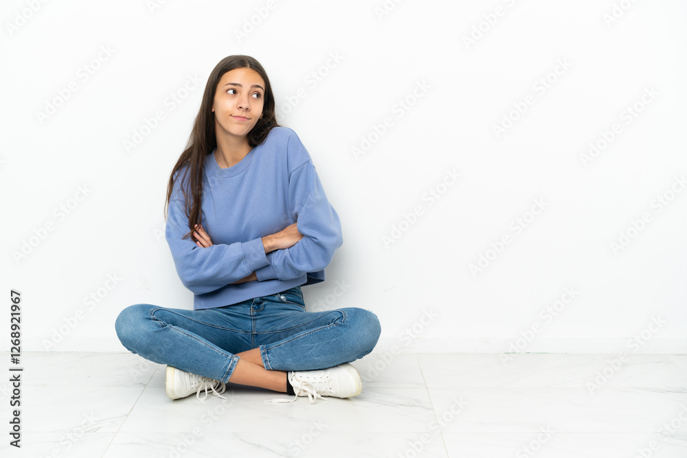Young French girl sitting on the floor making doubts gesture while lifting the shoulders Young French girl sitting on the floor making doubts gesture while lifting the shoulders