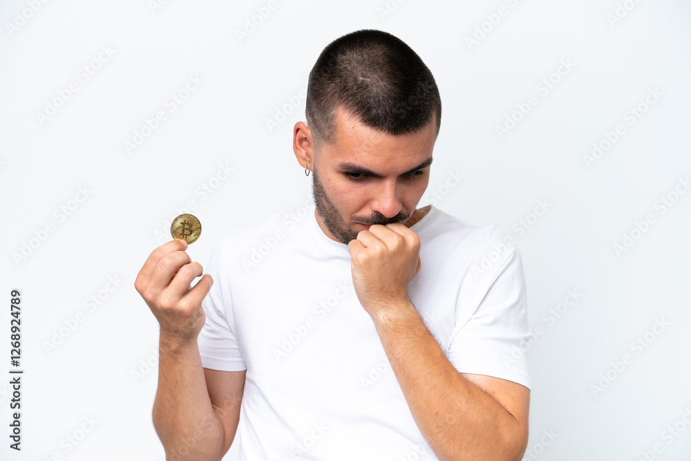 Young caucasian man holding a bitcoin isolated on white background having doubts Young caucasian man holding a bitcoin isolated on white background having doubts