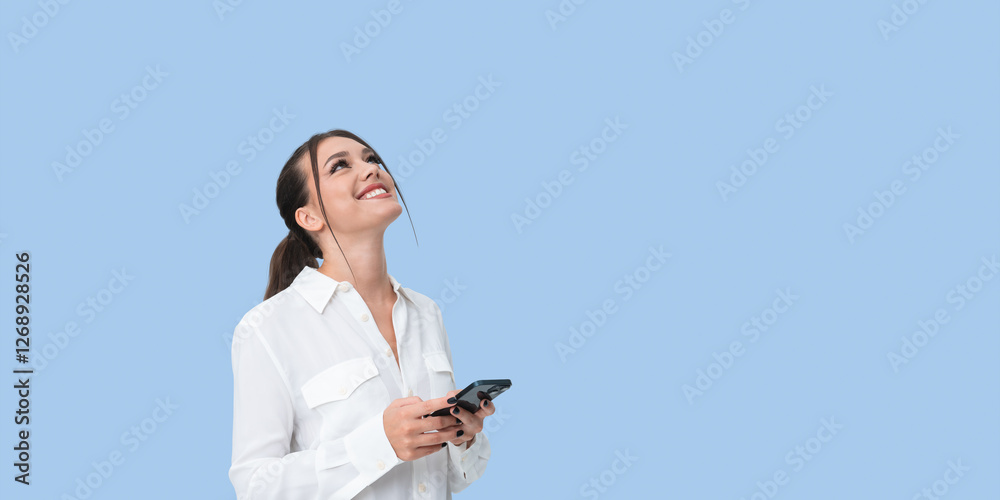 Smiling woman holding smartphone, looking upward on a light blue Smiling woman holding smartphone, looking upward on a light blue
