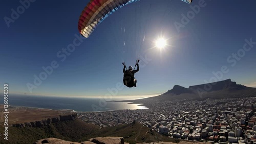 Aerial video captures a paraglider soaring over a coastal cityscape, with a wide-angle view highlighting the vibrant parachute and sunlit horizon.