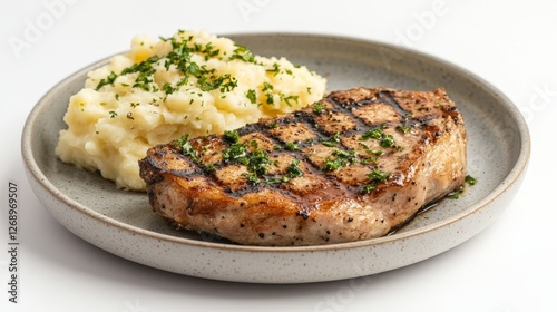 A plate featuring grilled pork chop and creamy mashed potatoes garnished with herbs.