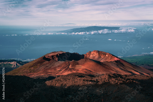 Impressive volcano crater of Pico Viejo with first sunshine during early morning in desert landscape with other Canary Islands and blue ocean on the background, Tenerife, Spain.