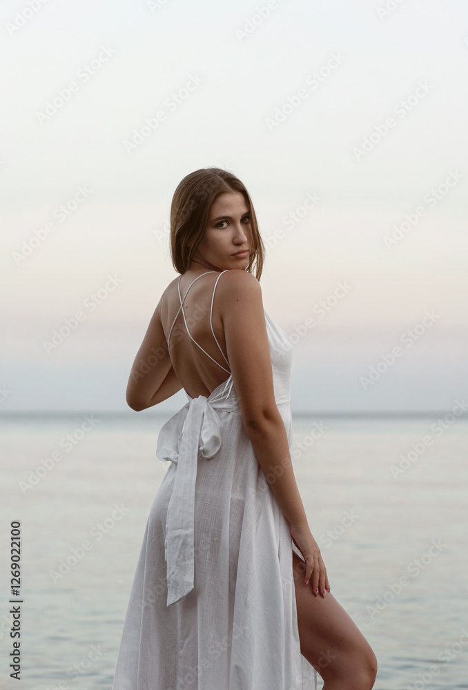 young girl in a long white dress against the sea. she has an open back young girl in a long white dress against the sea. she has an open back