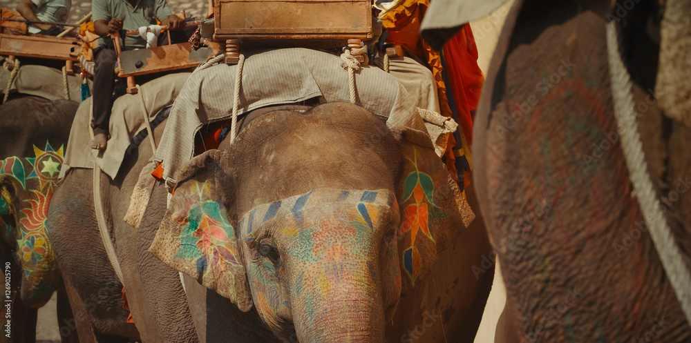 Jaipur, Rajasthan, India. Elephant Driver Sits On Elephant Walking Along City Street. Elephants Painted With Colorful Paints And Patterns. Busy Traffic On Narrow Street. Elephant Ride Is Tourist