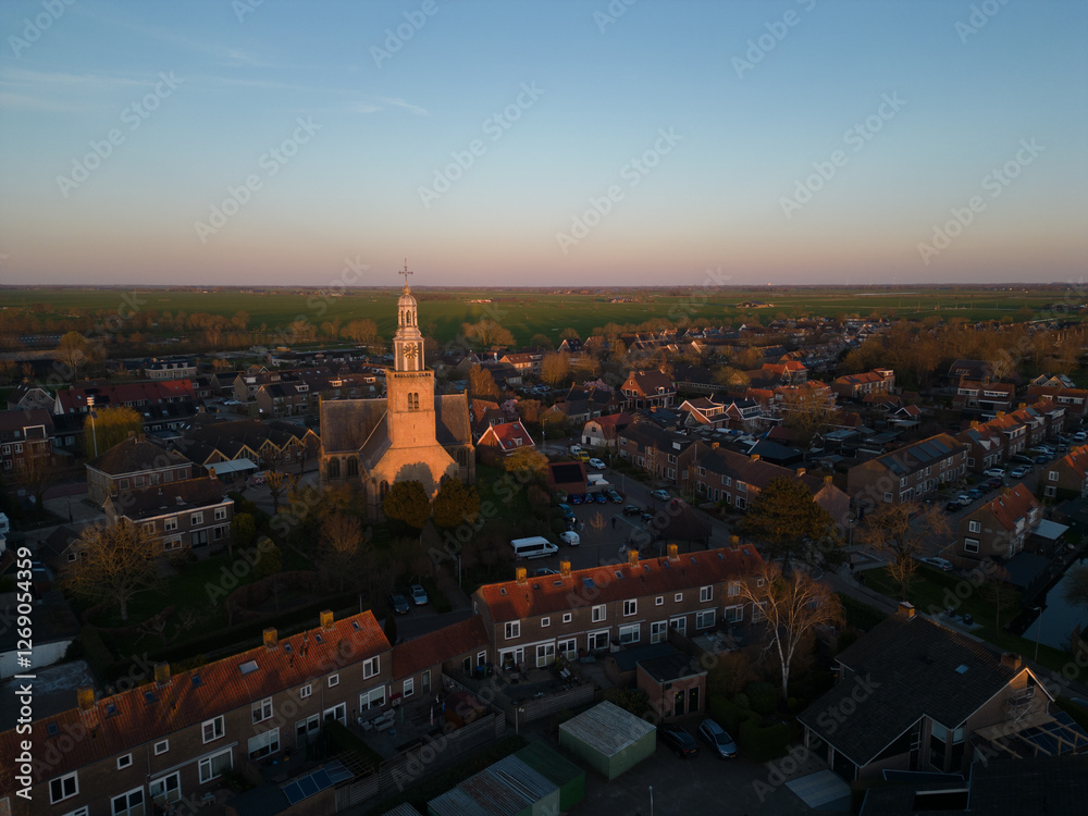Naklejka premium Aerial view of a Dutch Catholic church on the banks of the De Lek river in the southern Netherlands. Spring landscape with houses clustered on the vast plain of the Netherlands in the evening at sunse