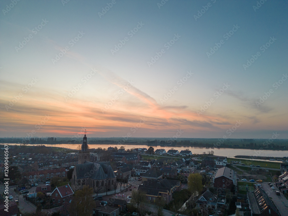 Naklejka premium Aerial view of a rural Dutch settlement on the banks of the De Lek river in the southern Netherlands. Spring landscape with houses clustered on the vast plain of Holland in the evening in Streefkerk