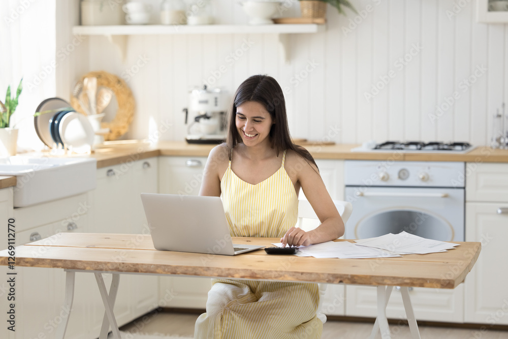 Budgeting and financial strategy. Smiling confident young female engaged in freelance accounting work at home office in kitchen planning finances balancing bills documents using calculator notebook Budgeting and financial strategy. Smiling confident young female engaged in freelance accounting work at home office in kitchen planning finances balancing bills documents using calculator notebook