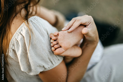 A mother gently cradles her baby’s foot, symbolizing love and tenderness
