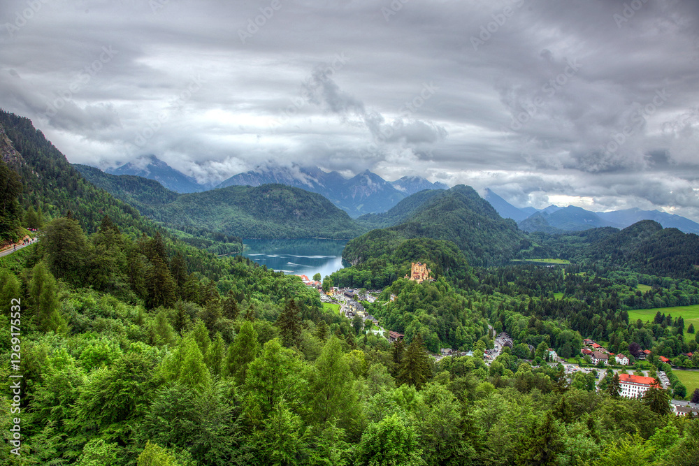 Fototapeta premium view of a castle in the mountains and a lake in bavaria germany. A mountain range with a lake in the middle. The lake is surrounded by trees. The mountains are covered in snow