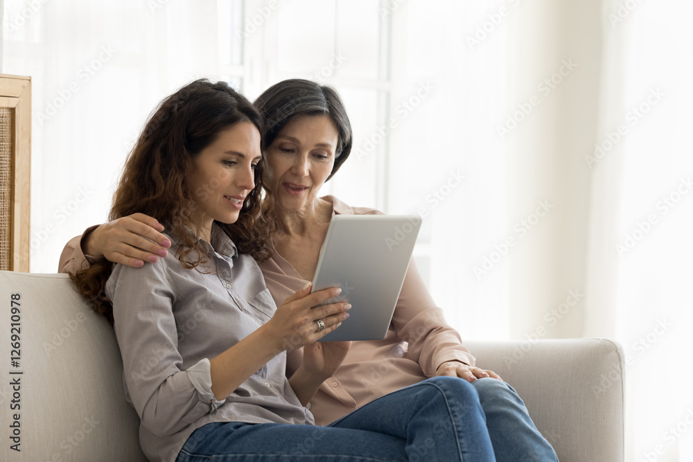 Digital age for all generations. Caring adult daughter sit on sofa with mature mom teach how to use tablet pc help to create social media account install photo video application show work of software