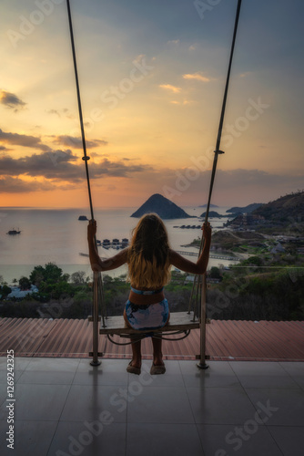 Obraz na płótnie A peaceful scene shows a person swinging joyfully at sunset over a shimmering ocean, with a distant tropical island, offering an escape from daily life, Komodo, Indonesia w salonie