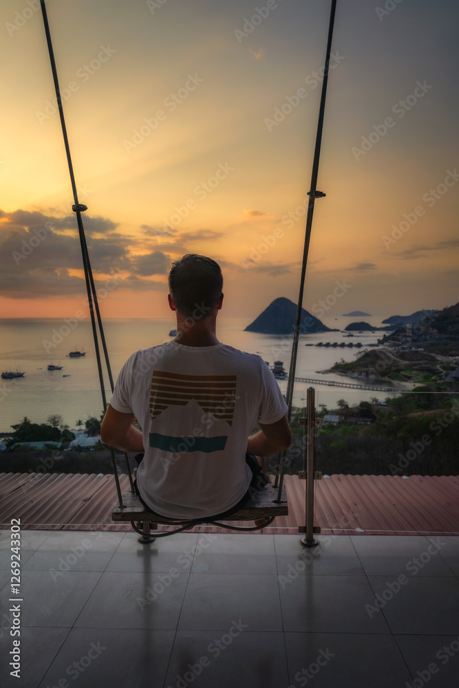 A person swings gently, absorbing the stunning sunsets beauty as it reflects over the ocean and hills, creating a moment of tranquility and relaxation, Komodo, Indonesia