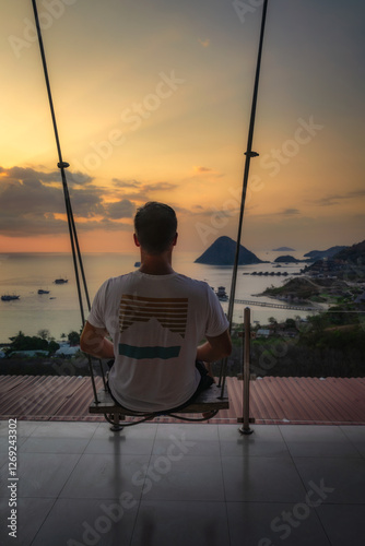 Obraz na płótnie A person swings gently, absorbing the stunning sunsets beauty as it reflects over the ocean and hills, creating a moment of tranquility and relaxation, Komodo, Indonesia w salonie
