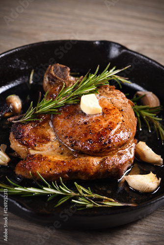 Pork cutlet on the bone in a piece of butter with garlic and rosemary in a frying pan 