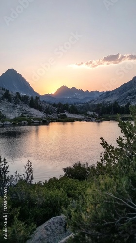 Sunset over a tranquil lake surrounded by mountains with vibrant colors refle...