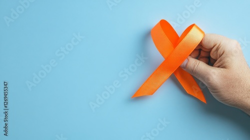 Hand holding orange awareness ribbon against blue background photo