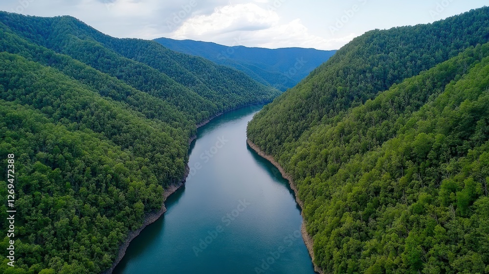 Aerial view of a serene river winding through a lush green valley, surrounded by steep hills under a partly cloudy sky. The water is dark blue Aerial view of a serene river winding through a lush green valley, surrounded by steep hills under a partly cloudy sky. The water is dark blue