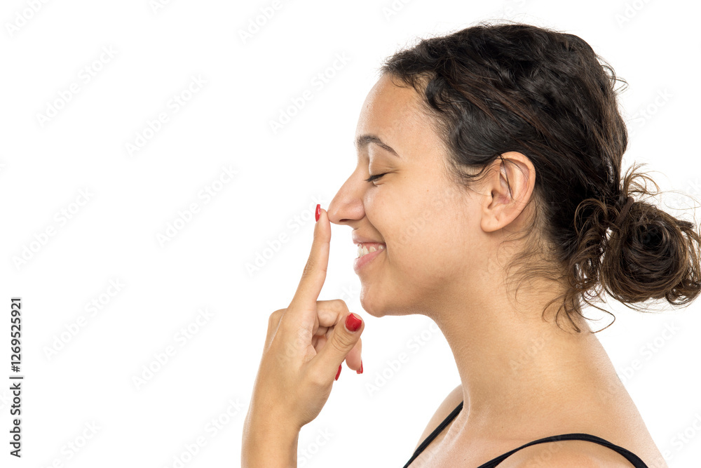 Profile view of young woman touching nose, smiling. Natural appearance, no makeup, dark curly hair in bun. Rhinoplasty concept. Studio portrait on white background. Profile view of young woman touching nose, smiling. Natural appearance, no makeup, dark curly hair in bun. Rhinoplasty concept. Studio portrait on white background.