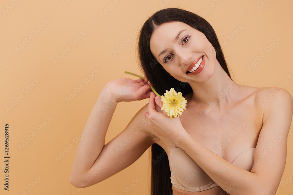 Beautiful smiling woman holding yellow gerbera flower and playing with her hair on a beige background. Beautiful smiling woman holding yellow gerbera flower and playing with her hair on a beige background.