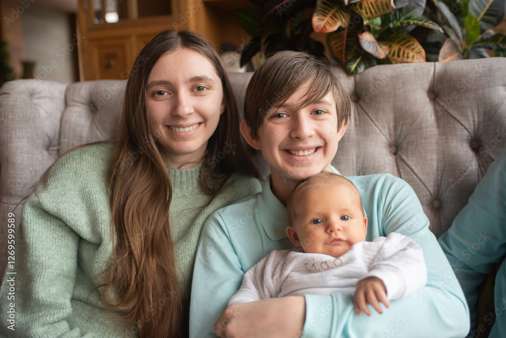 Smiling siblings, two teenagers and a baby. Brother holding younger brother and sitting next to older sister. Smiling siblings, two teenagers and a baby. Brother holding younger brother and sitting next to older sister.