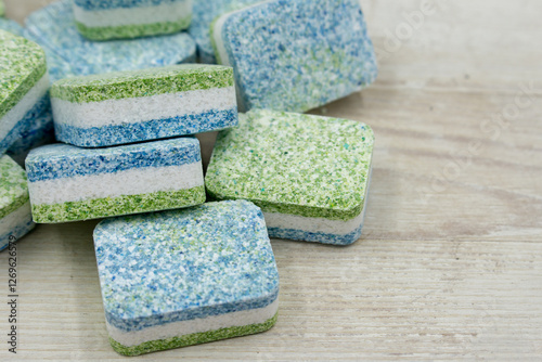 Dishwasher tablets on white wooden background.