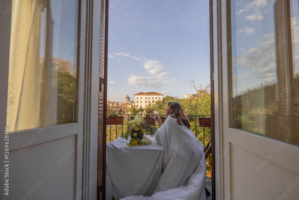 A woman wrapped in a soft white blanket enjoys a peaceful morning on a charming balcony in Rome, overlooking St Peters Basilica
