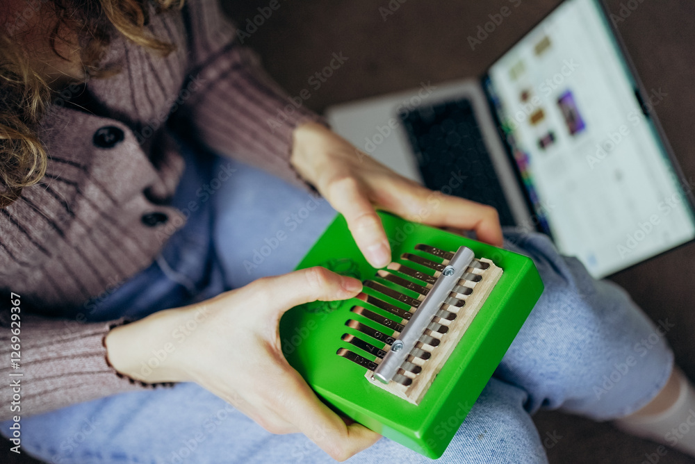 Woman playing a vibrant green kalimba while engaging in an online course on her laptop, immersing herself in the joy of learning and exploring a new musical hobby Woman playing a vibrant green kalimba while engaging in an online course on her laptop, immersing herself in the joy of learning and exploring a new musical hobby