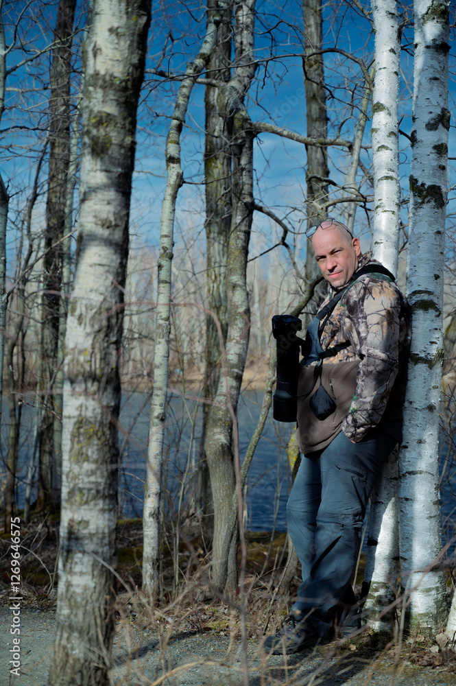 Obraz premium A man with a camera, with a hunting coat is resting in a birch grove