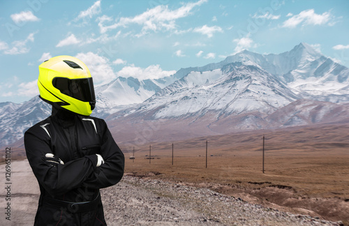 A man motorcyclist biker wearing a yellow helmet stands in the desert with his arms crossed