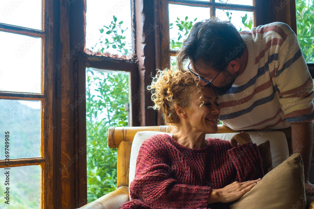 © simona - Adult man and woman sharing a romantic kiss while cuddling in a cozy mountain home, enjoying a peaceful and intimate moment together, feeling deep emotional connection, love, and happiness