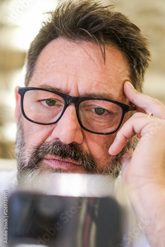 Man sitting at home, looking at his phone with a serious expression while reading a phishing scam notification. He struggles to comprehend the message, feeling confusion as he browses the web